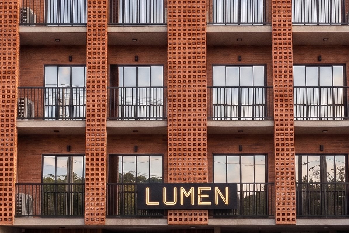 Detalle de la fachada de Lumen Studios: celosías de ladrillo, balcones con barandas negras y el cartel LUMEN iluminado